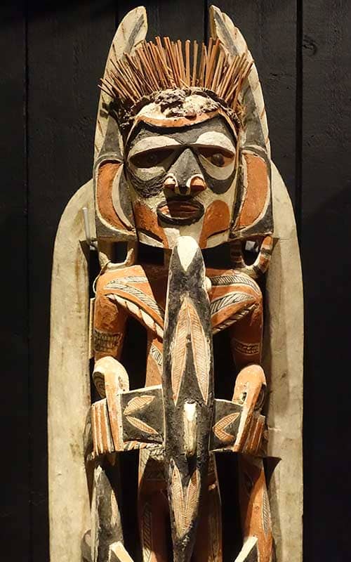 An imposing wooden Malagan sculpture of a figure in shades or dark brown and orange