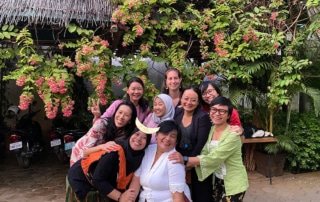 Group of women smile in front of a tree with pink flowers