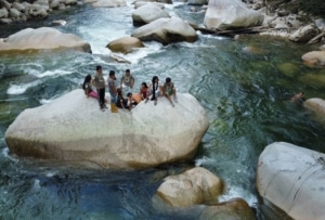 A group of people sitting on a rock in a river.