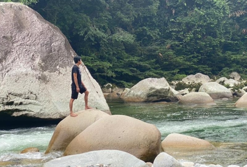 Young man stands on large rock mid-river