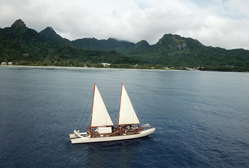 A traditional vacca voyage vessel at sea with land behind