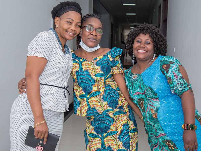 Three women participants smile at the camera at a conference organised in Kinshasa to bring Synchronicity Earth partners together