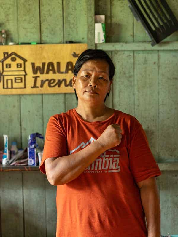 A woman in an orange t-shirt holds her arm across her chest and looks at the camera