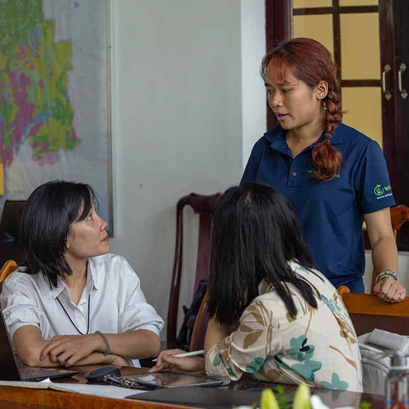 One woman standing up talks to two women sitting down during a training workshop