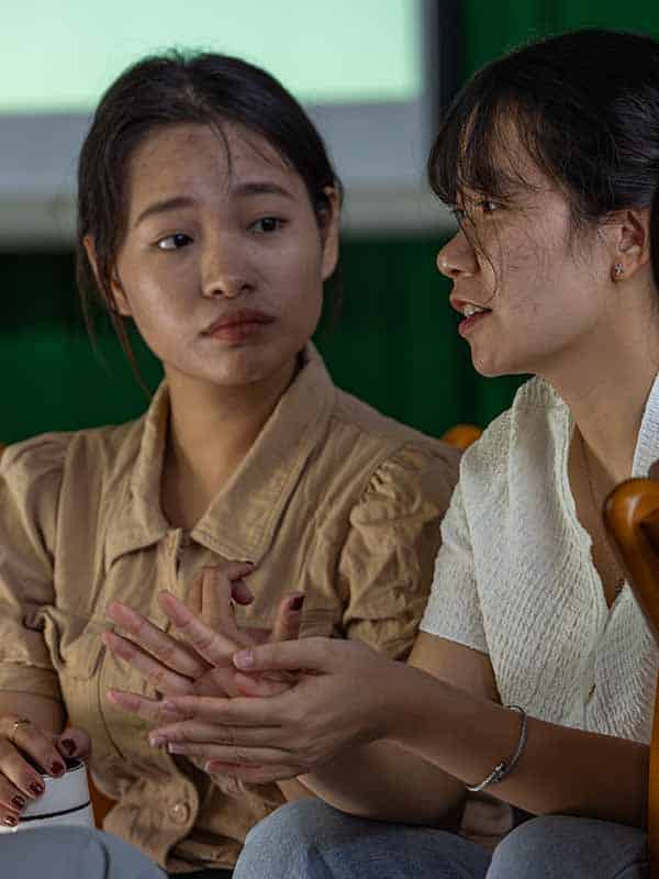 Two women sat next to each other during a workshop, one explaining while the other listens